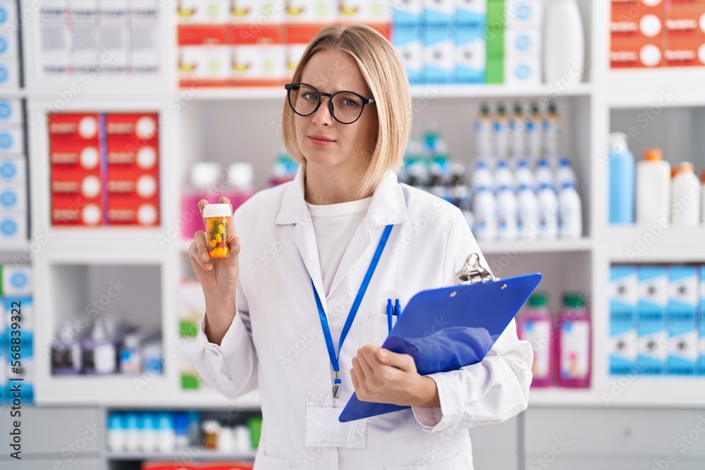 Young caucasian woman working at pharmacy drugstore holding pills skeptic and nervous, frowning upset because of problem. negative person.