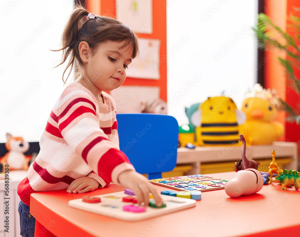 Fototapeta premium Adorable hispanic girl playing with maths puzzle game standing at kindergarten