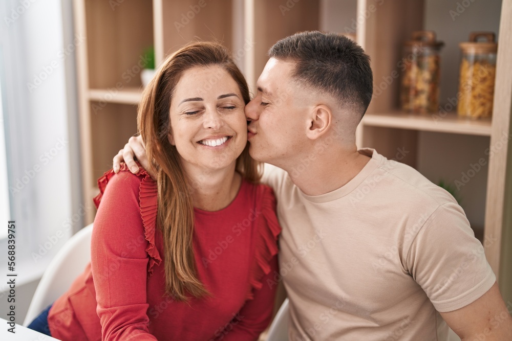 Man and woman mother and son hugging each other and kissing sitting on table at home Man and woman mother and son hugging each other and kissing sitting on table at home