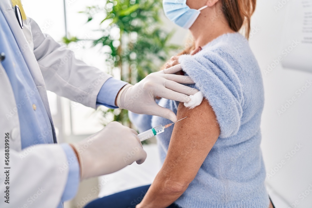 Middle age man and woman doctor vaccinating patient at clinic Middle age man and woman doctor vaccinating patient at clinic