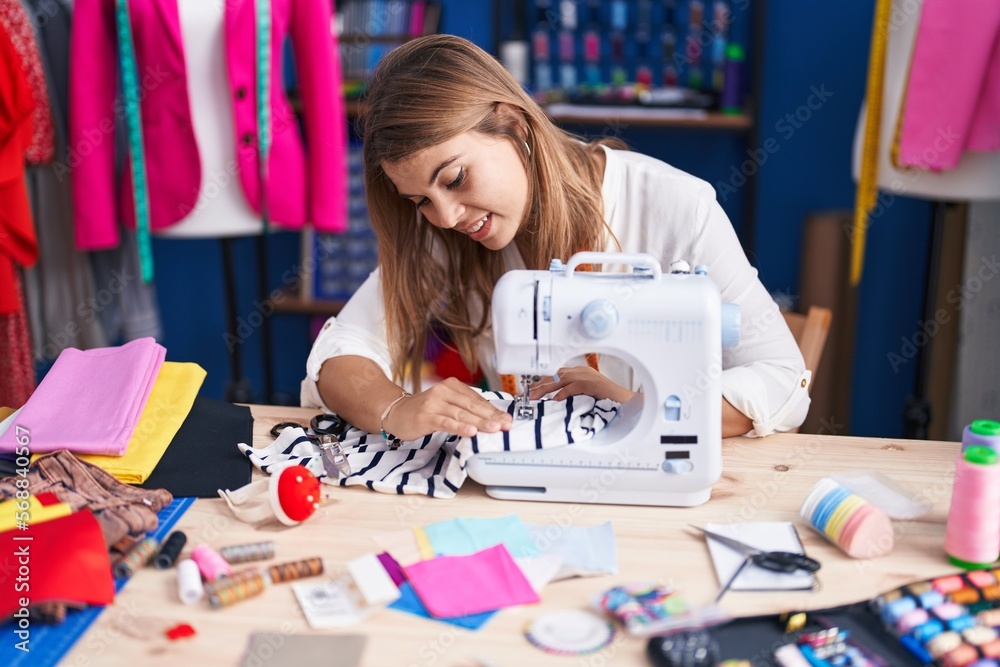 Fototapeta premium Young woman tailor smiling confident using sewing machine at sewing studio