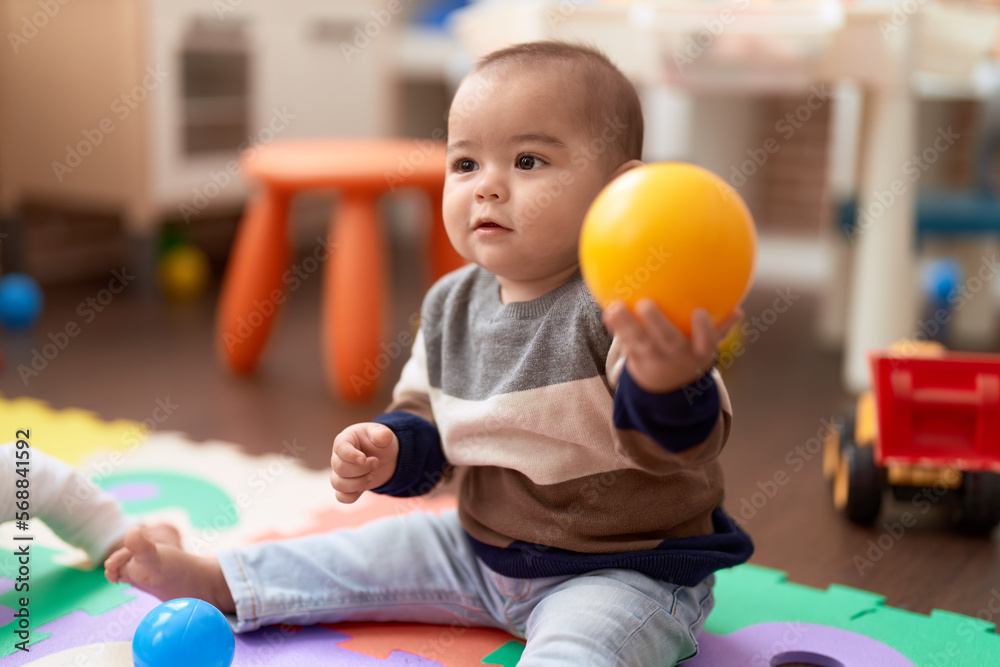 Adorable chinese toddler playing with ball sitting on floor at kindergarten Adorable chinese toddler playing with ball sitting on floor at kindergarten