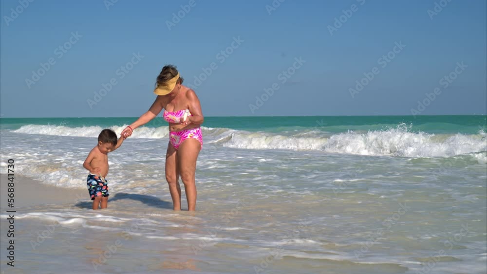 Young little latin boy enjoying the beach and the waves with his grandmother on a sunny afternoon Young little latin boy enjoying the beach and the waves with his grandmother on a sunny afternoon