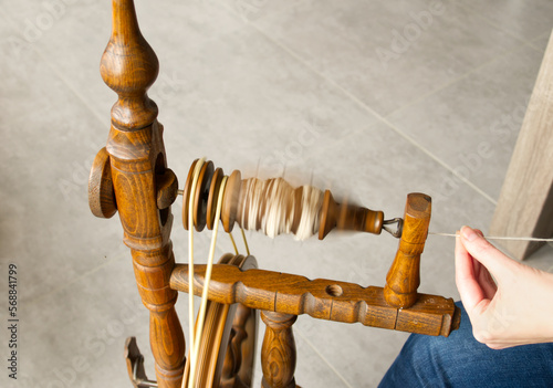 Close-up of wool being spun onto the bobbin of an old, castle-style spinning wheel. The spinner's hands can be seen drafting the fiber. The motion of the bobbin is blurred.