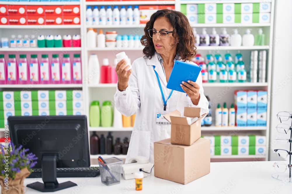 Middle age woman pharmacist using touchpad holding pills bottle at pharmacy
