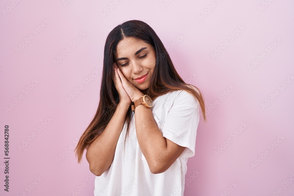 Young arab woman standing over pink background sleeping tired dreaming and posing with hands together while smiling with closed eyes. Young arab woman standing over pink background sleeping tired dreaming and posing with hands together while smiling with closed eyes.