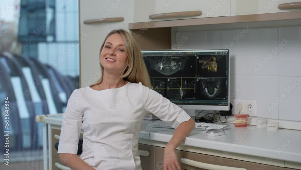 A woman dentist in a white suit looks at a computer snapshot of the jaw A woman dentist in a white suit looks at a computer snapshot of the jaw