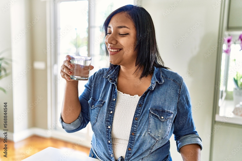 Hispanic brunette woman drinking a glass of water at the kitchen Hispanic brunette woman drinking a glass of water at the kitchen