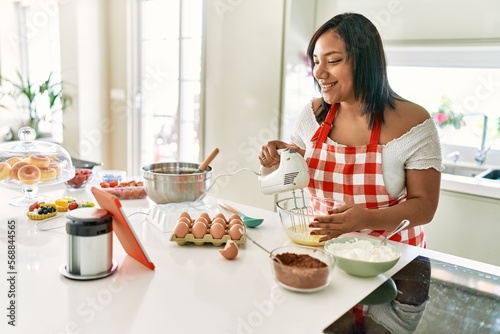 Hispanic brunette woman preparing cake looking at online recipe at the kitchen