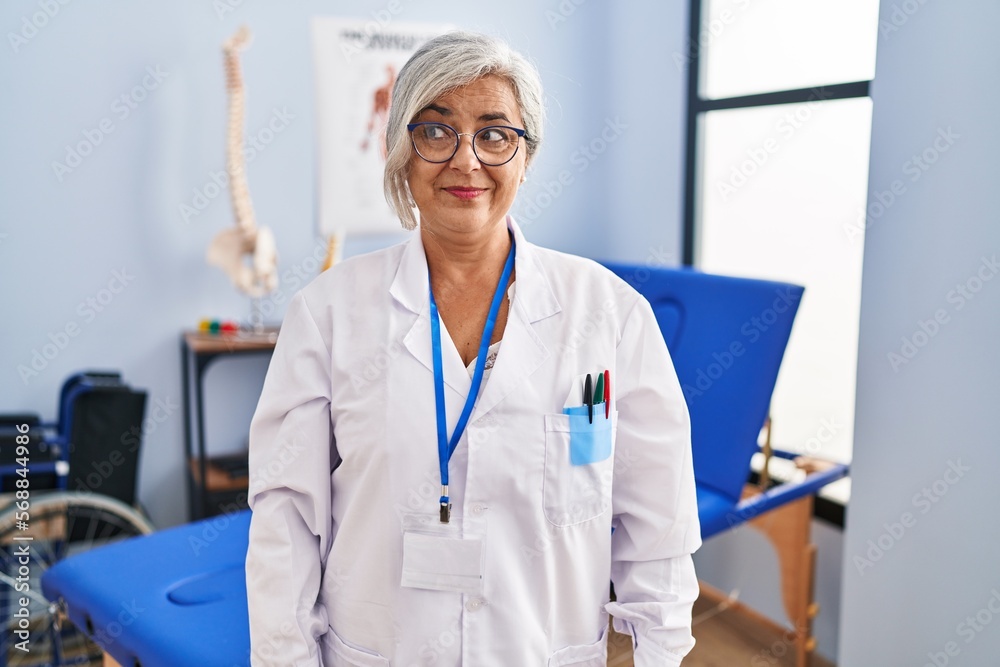 Middle age woman with grey hair working at pain recovery clinic smiling looking to the side and staring away thinking. Middle age woman with grey hair working at pain recovery clinic smiling looking to the side and staring away thinking.