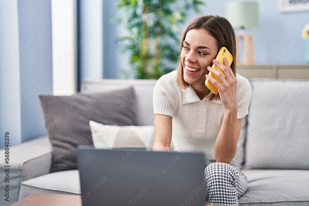 Young beautiful hispanic woman talking on smartphone using laptop at home Young beautiful hispanic woman talking on smartphone using laptop at home
