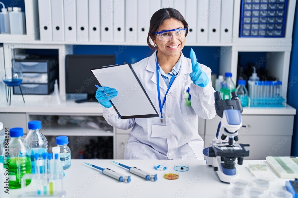 Hispanic young woman working at scientist laboratory pointing fingers to camera with happy and funny face. good energy and vibes.