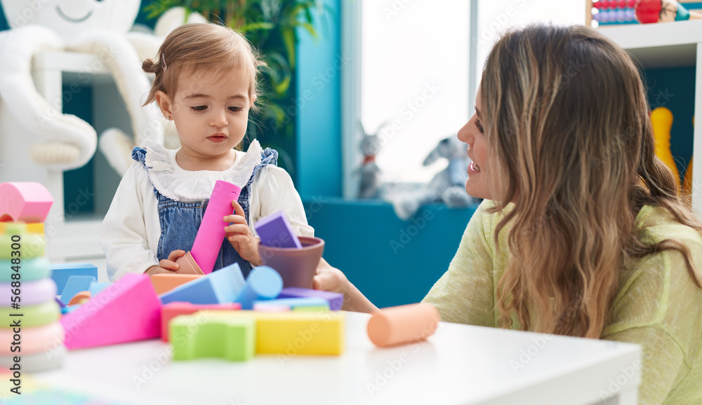 Teacher and toddler playing with geometry blocks sitting on table at kindergarten Teacher and toddler playing with geometry blocks sitting on table at kindergarten