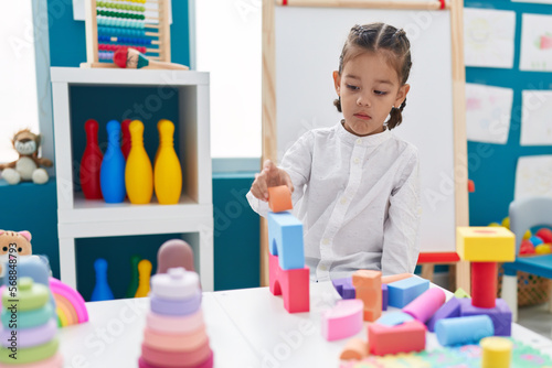 Adorable hispanic boy playing with construction blocks standing at kindergarten