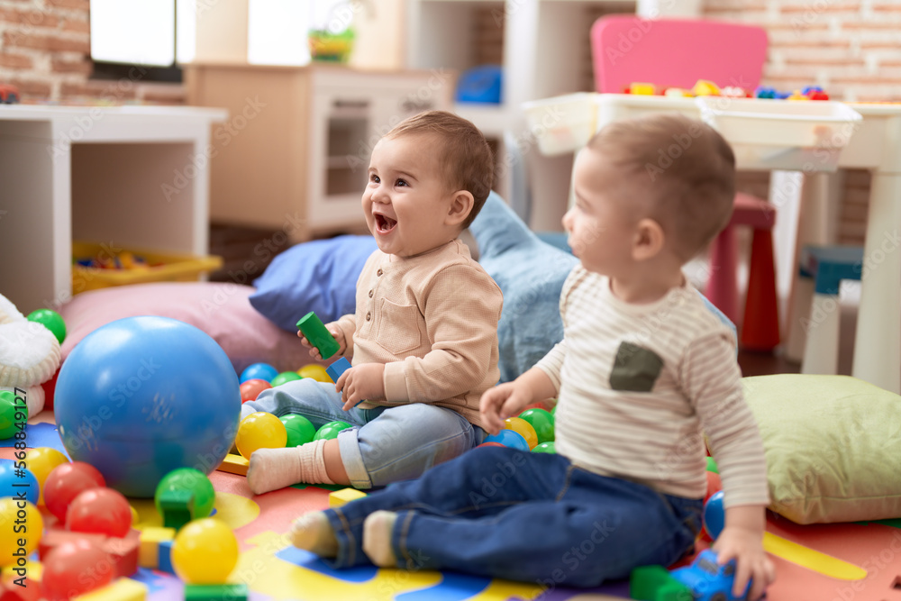 Two adorable toddlers playing with balls sitting on floor at kindergarten Two adorable toddlers playing with balls sitting on floor at kindergarten