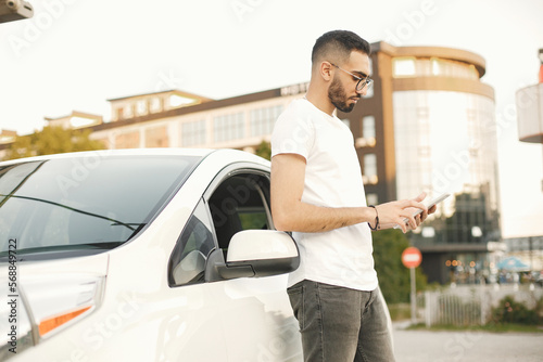Male driver using a phone while standing near his car