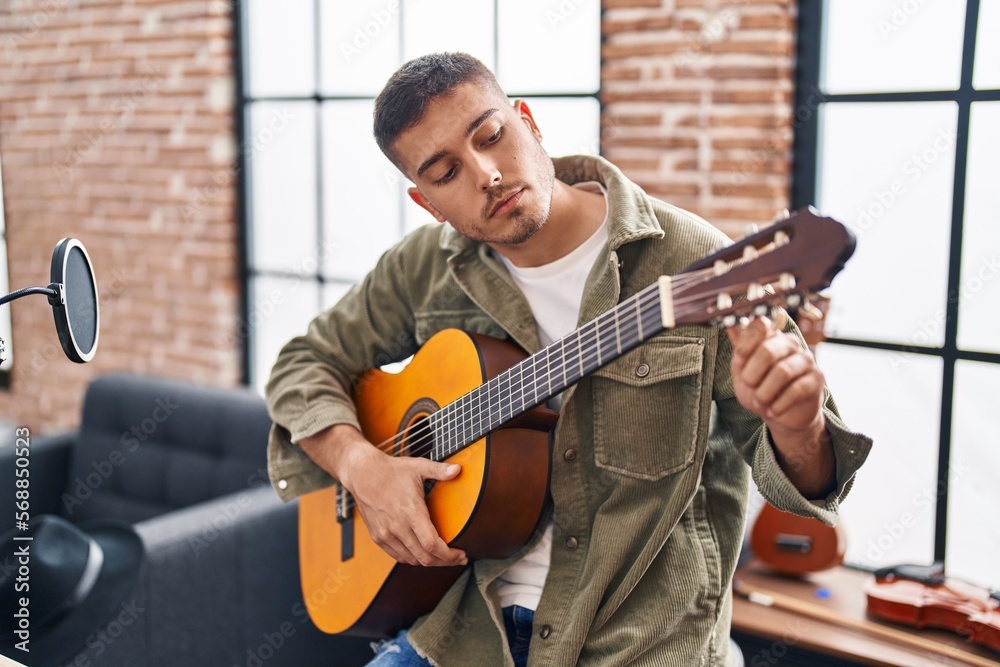 Obraz premium Young hispanic man musician playing classical guitar at music studio