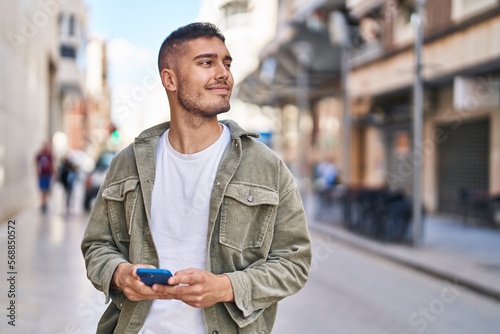 Young hispanic man smiling confident using smartphone at street