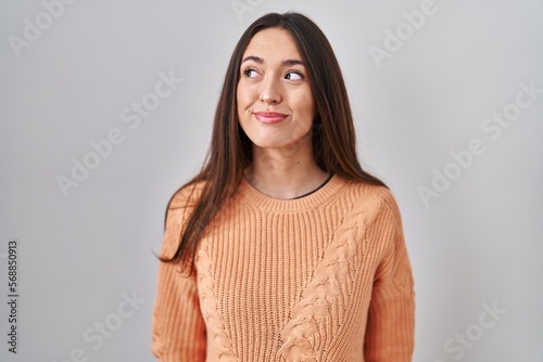 Young brunette woman standing over white background smiling looking to the side and staring away thinking.