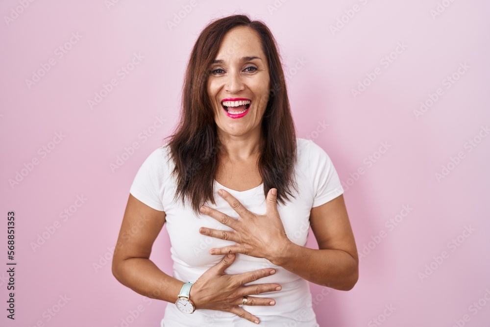 Middle age brunette woman standing over pink background smiling and laughing hard out loud because funny crazy joke with hands on body. Middle age brunette woman standing over pink background smiling and laughing hard out loud because funny crazy joke with hands on body.