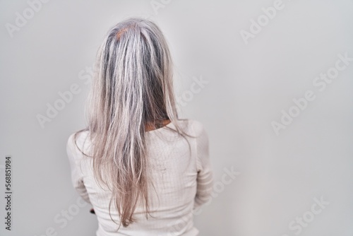 Middle age woman with grey hair standing over white background standing backwards looking away with crossed arms