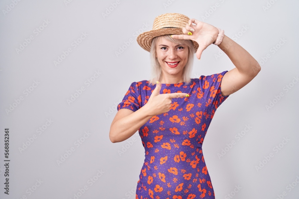 Young caucasian woman wearing flowers dress and summer hat smiling making frame with hands and fingers with happy face. creativity and photography concept. Young caucasian woman wearing flowers dress and summer hat smiling making frame with hands and fingers with happy face. creativity and photography concept.