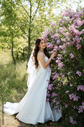 young girl bride in a white dress in a spring forest in lilac bushes
