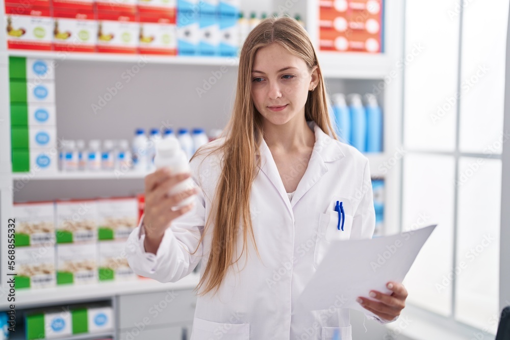 Young caucasian woman pharmacist holding pills bottle reading prescription at pharmacy