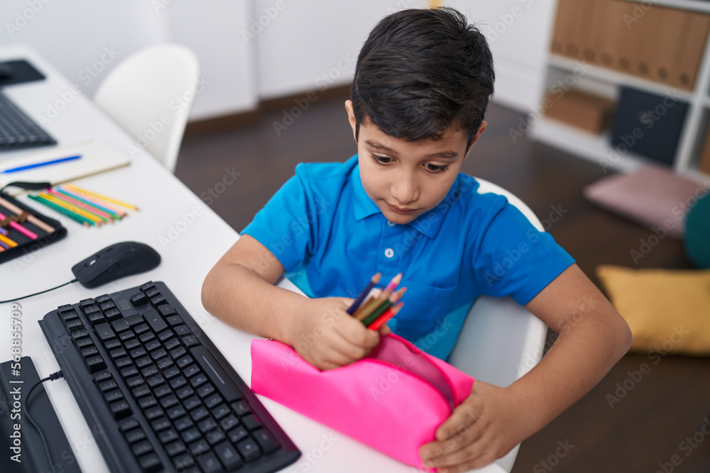 Adorable hispanic boy student holding pencil of case at classroom Adorable hispanic boy student holding pencil of case at classroom