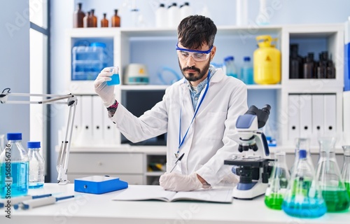 Young hispanic man scientist writing on notebook measuring liquid at laboratory