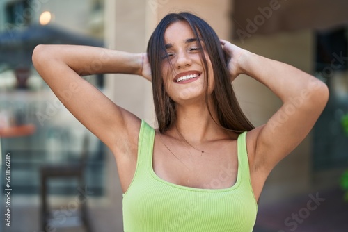 Young beautiful hispanic woman smiling confident relaxed with hands on head and closed eyes at street