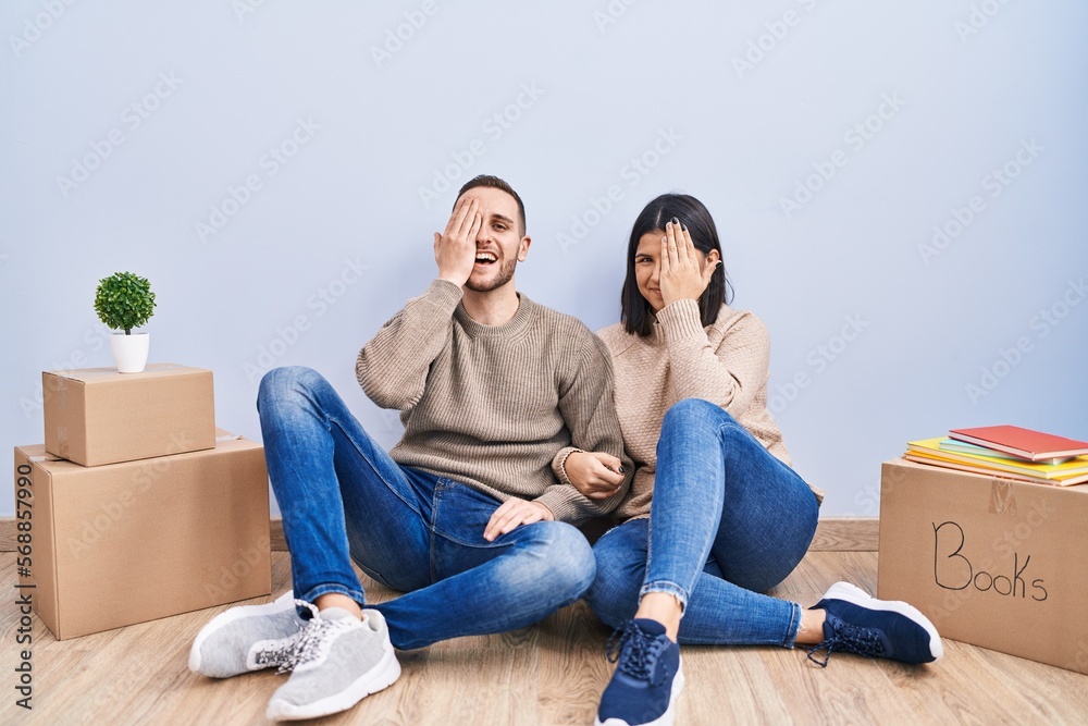 Young couple moving to a new home covering one eye with hand, confident smile on face and surprise emotion. Young couple moving to a new home covering one eye with hand, confident smile on face and surprise emotion.