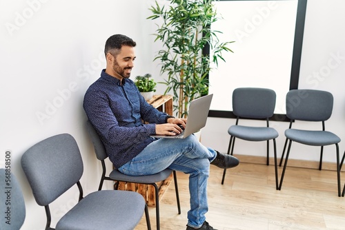 Young hispanic man using laptop sitting on chair at waiting room