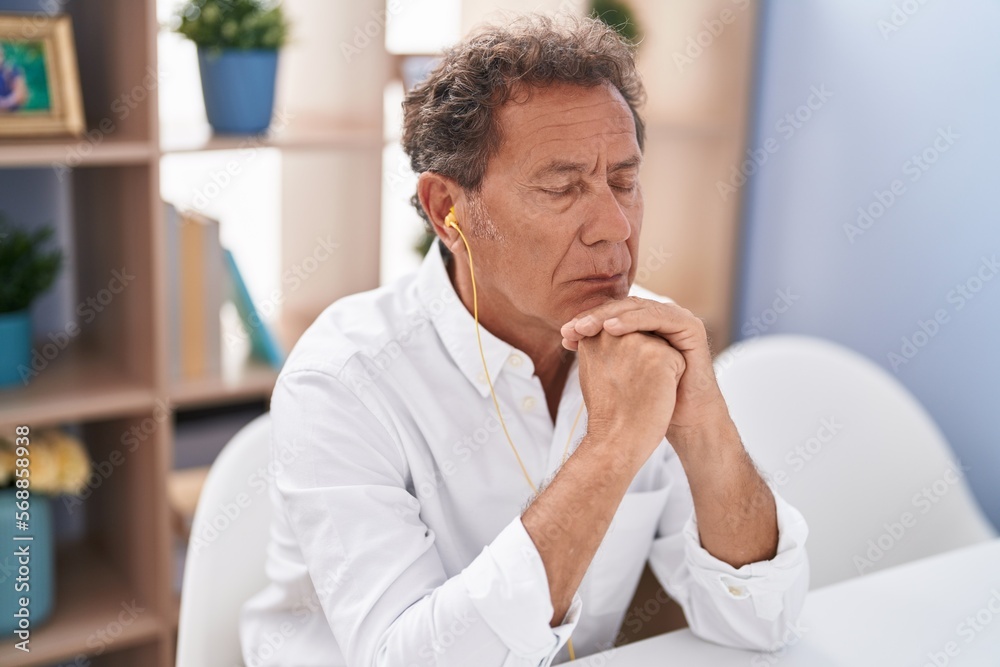 Naklejka premium Middle age man listening to music sitting on table at home