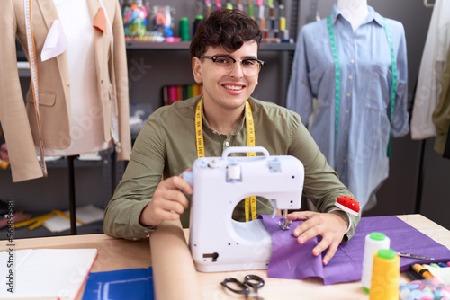 Non binary man tailor smiling confident using sewing machine at atelier