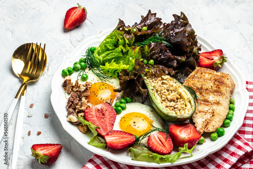 Healthy nutritious paleo keto breakfast diet Fried eggs, avocado, grilled chicken fillet, nuts, strawberries and fresh salad. Keto breakfast or lunch. top view