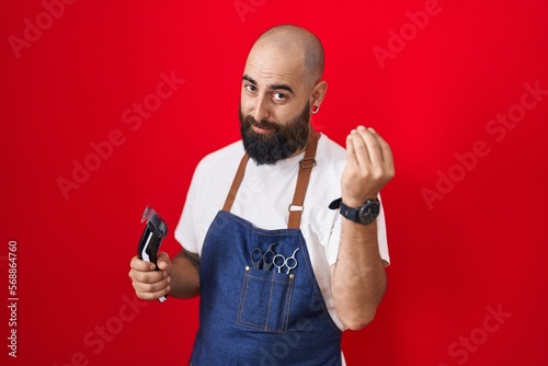 Young hispanic man with beard and tattoos wearing barber apron holding razor doing italian gesture with hand and fingers confident expression © Krakenimages.com