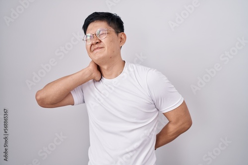 Young asian man standing over white background suffering of neck ache injury, touching neck with hand, muscular pain