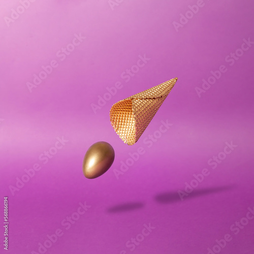 Surreal scene with golden egg and ice cream cone against deep purple background. Creative easter composition.
