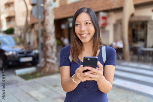Young asian woman smiling confident using smartphone at street