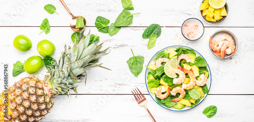 Fresh pineapple salad with shrimps, spinach, avocado and lime on white kitchen table, top view. Healthy eating, balanced, clean diet food, weight loss concept, banner