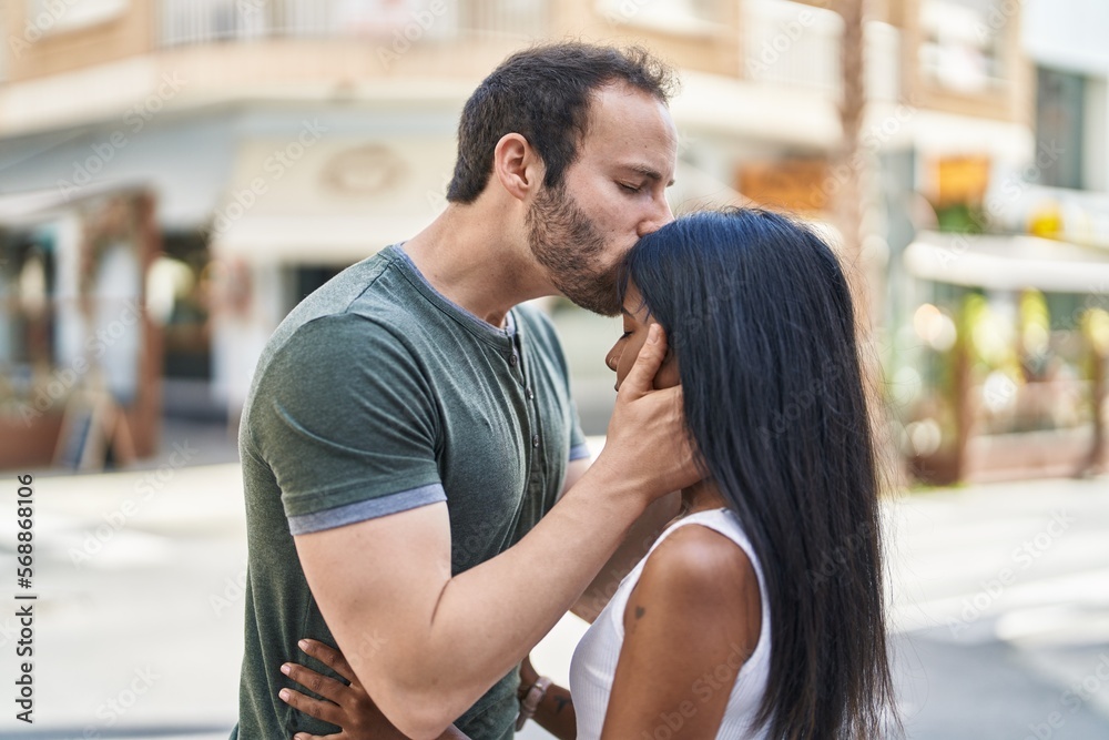Man and woman interracial couple hugging each other and kissing at street