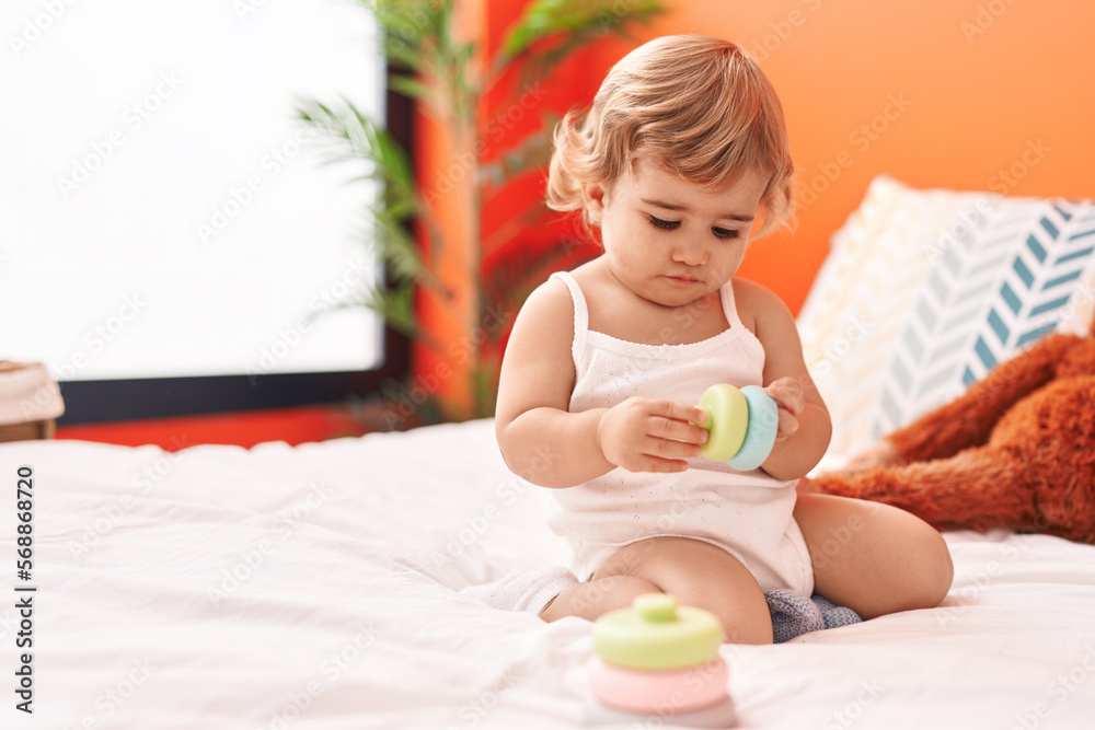 Adorable hispanic toddler playing with toy sitting on bed at bedroom Adorable hispanic toddler playing with toy sitting on bed at bedroom