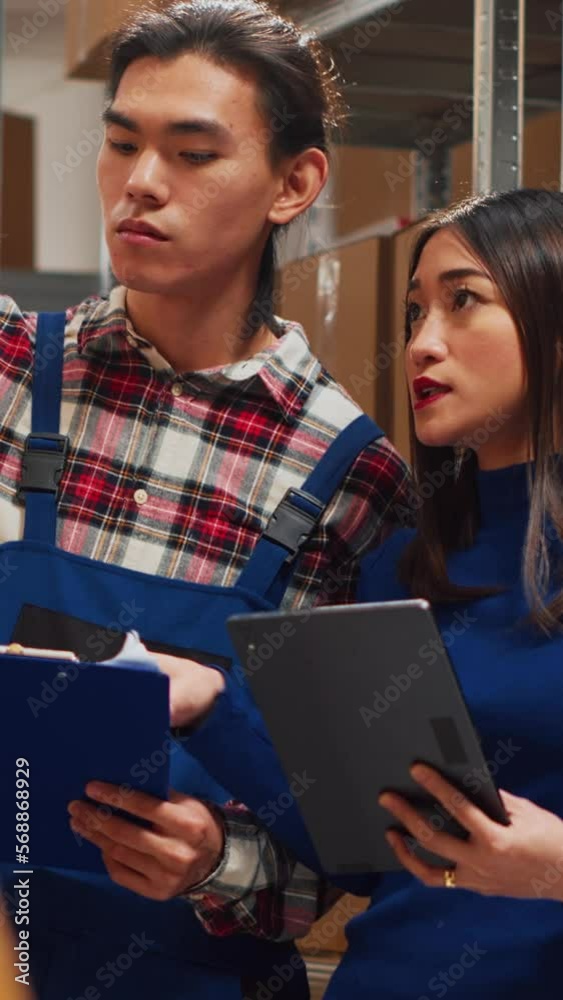 Vertical video: Asian people analyzing stock with tablet and papers, working on products distribution for business development. Team of employees organizing merchandise and supplies. Handheld shot. Vertical video: Asian people analyzing stock with tablet and papers, working on products distribution for business development. Team of employees organizing merchandise and supplies. Handheld shot.