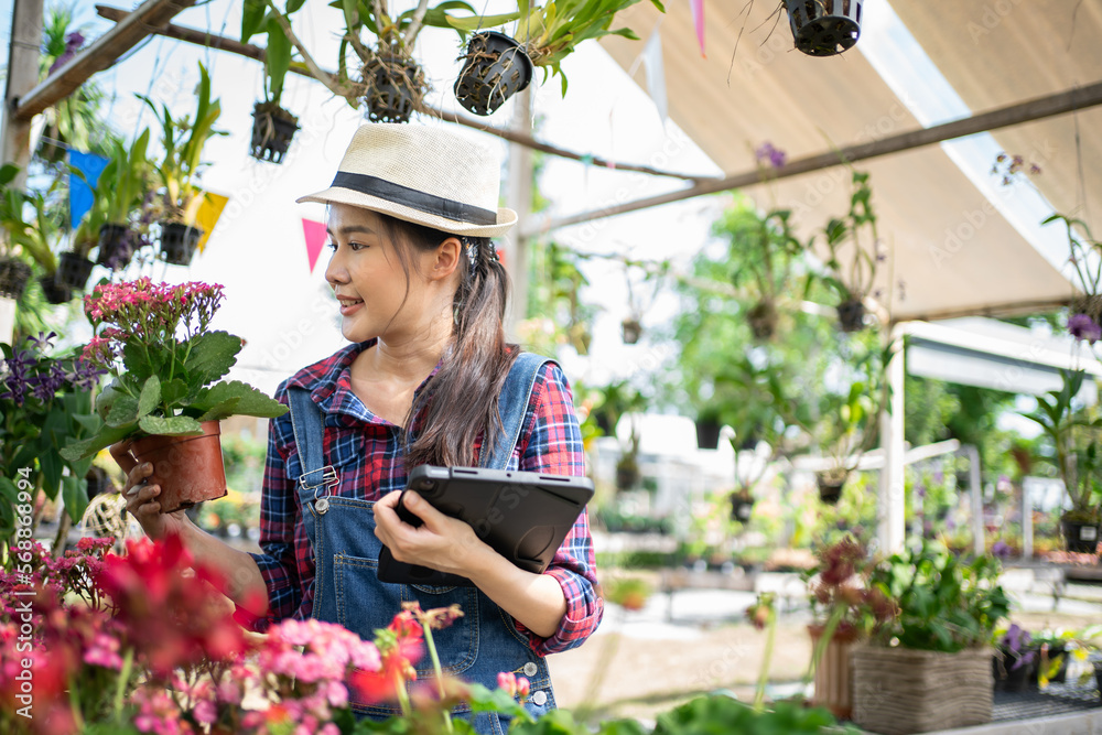 Modern technology in gardening business. Portrait of Asian female environmentalist using digital tablet in garden. Confident female is wearing apron while working.