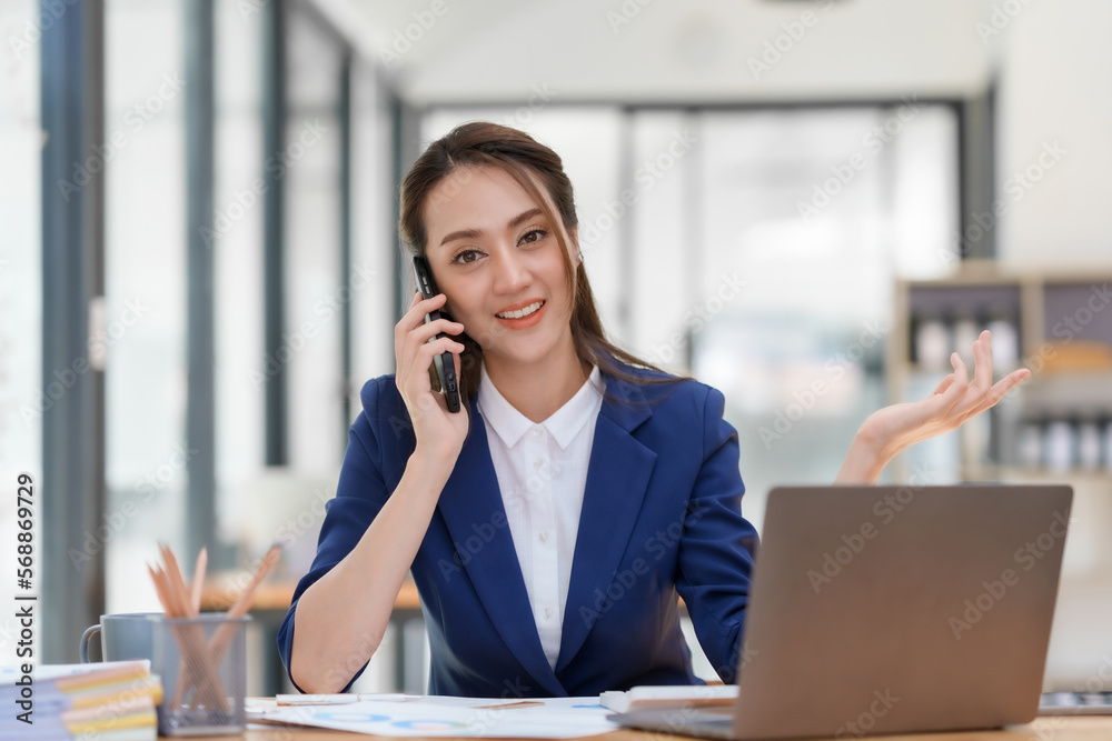 Beautiful smiling Asian businesswoman talking on mobile phone while working in office. Beautiful smiling Asian businesswoman talking on mobile phone while working in office.
