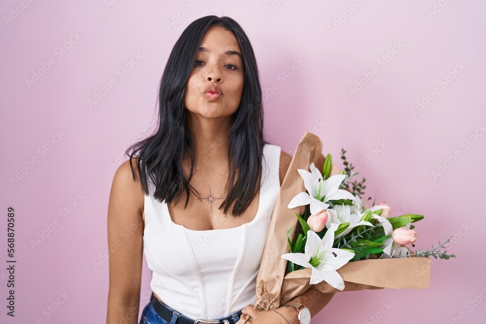 Brunette woman holding bouquet of white flowers looking at the camera blowing a kiss on air being lovely and sexy. love expression. Brunette woman holding bouquet of white flowers looking at the camera blowing a kiss on air being lovely and sexy. love expression.