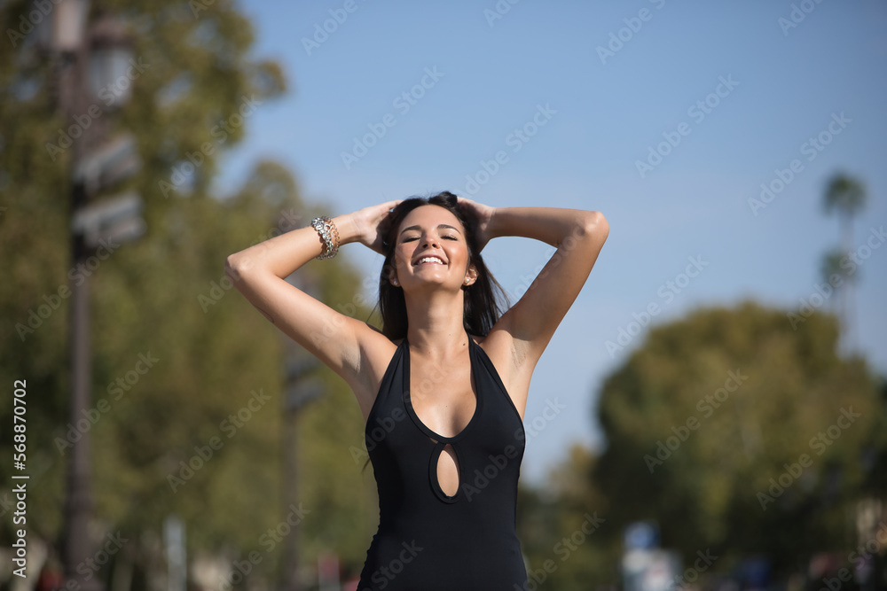 Beautiful young woman with straight brown hair, wearing an elegant black dress, touching her hair in sensual and seductive attitude. Concept fashion, beauty, sensuality, provocation, millennial.