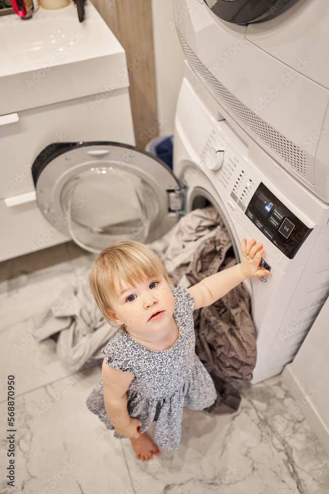 House cleaning. Happy baby girl one and a half, helper are having fun and smiling while in a bright apartment. Helps parents change bed linen and do laundry in the washing machine. House cleaning. Happy baby girl one and a half, helper are having fun and smiling while in a bright apartment. Helps parents change bed linen and do laundry in the washing machine.