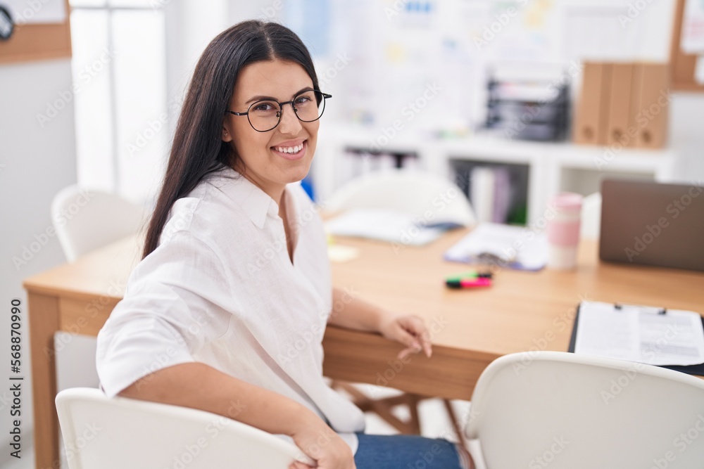 Young beautiful hispanic woman business worker smiling confident sitting on table at office Young beautiful hispanic woman business worker smiling confident sitting on table at office